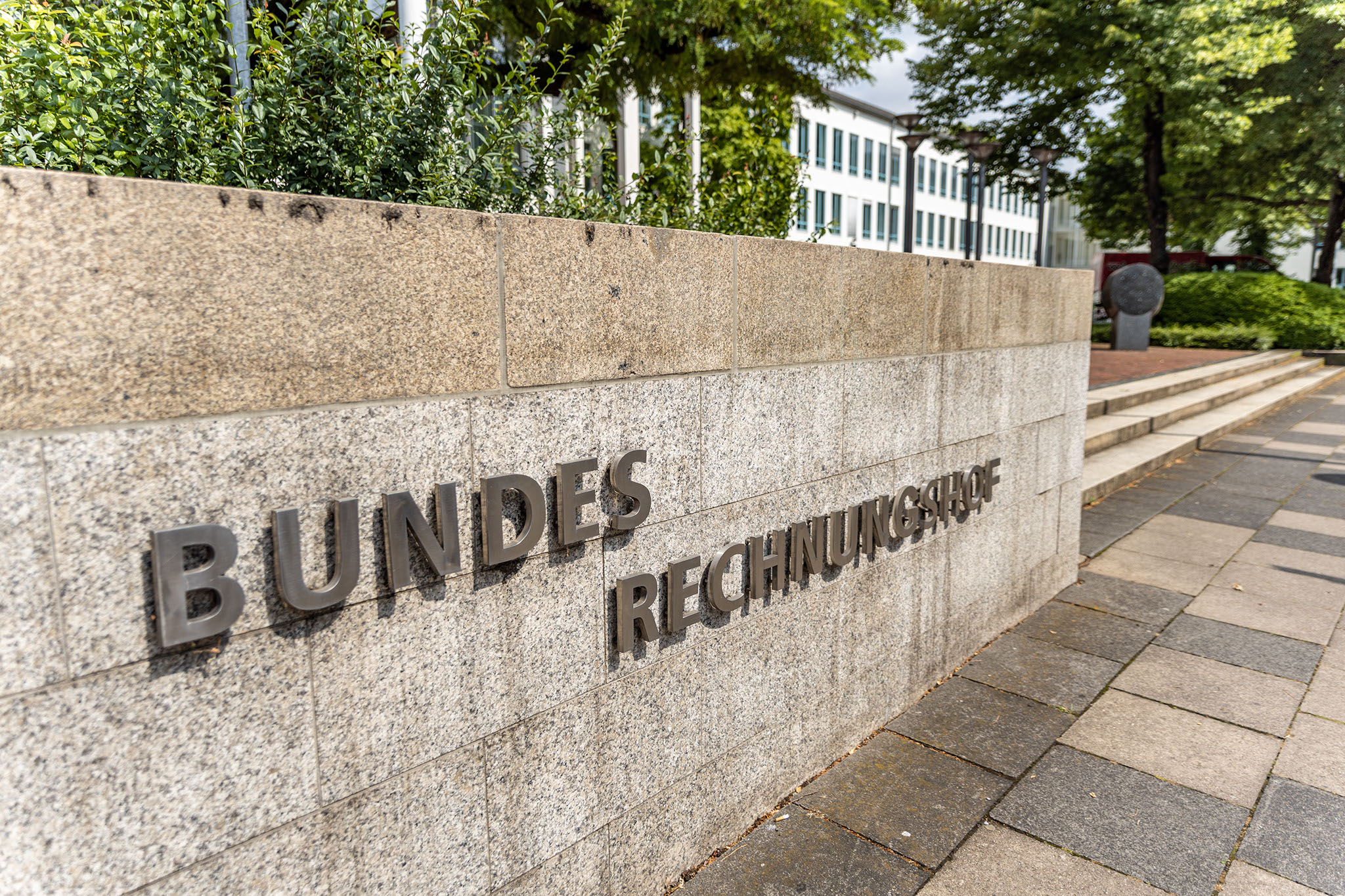 Das Foto zeigt eine graue Steinmauer mit Schriftzug Bundesrechnungshof am Haupteingang des Bundesrechnungshofes in Bonn. Quelle: Nadine Normann, Fotografie & Design.
